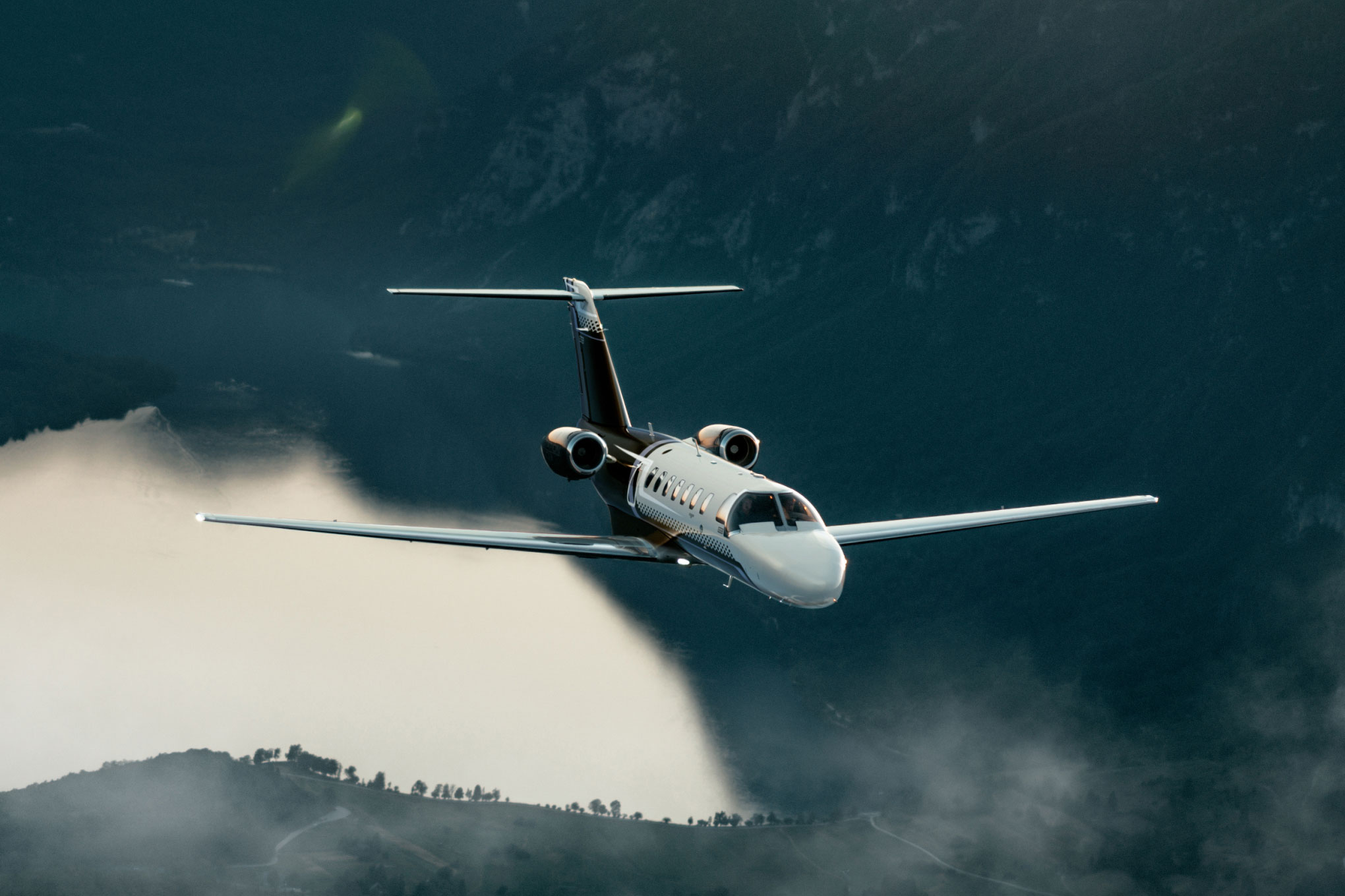 Cessna Citation CJ3 in flight above low cloud and forested hills