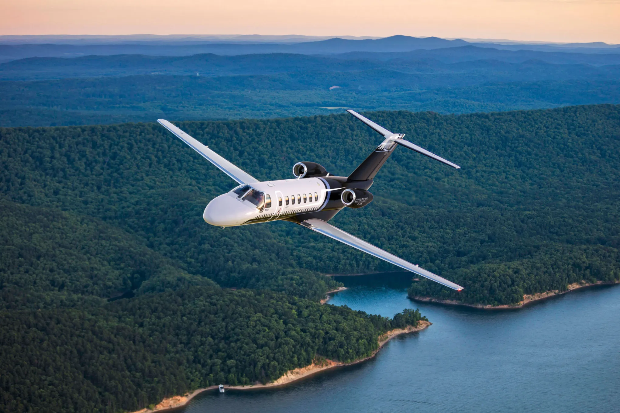 Cessna Citation CJ3 in flight over wooded hills and a reservoir