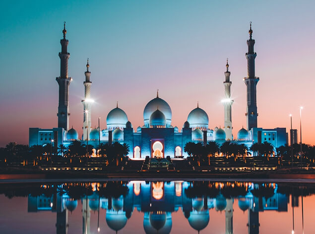 Abu Dhabi: The Sheikh Zayed Grand Mosque lit blue at dusk, its white domes and minarets mirrored in the reflecting pool