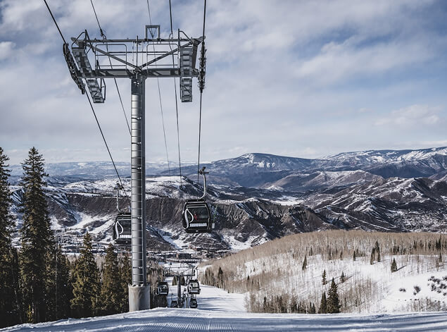 Aspen: A gondola line climbing over snow-covered pistes and pine, with the Elk Mountains beyond