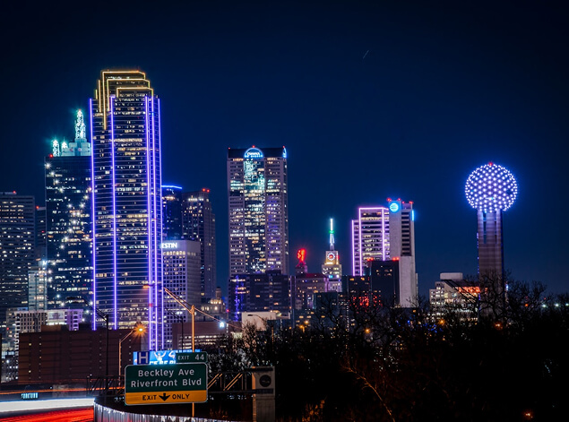 Dallas: The Dallas skyline at night in neon blue and violet, Reunion Tower at right above a lit highway sign