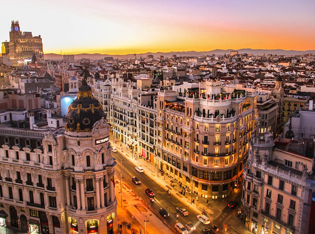 Madrid: The Gran Vía at sunset from above, the domed Metropolis building among lit facades and traffic