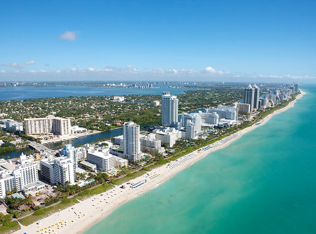 Miami: An aerial along South Beach, the hotel strip in a white line between turquoise shallows and the bay