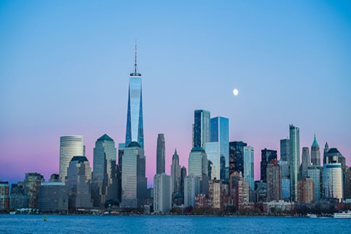 New York: Lower Manhattan across the harbour at dusk, One World Trade Center tallest, a moon above the skyline