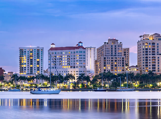 Palm Beach: Mediterranean-style resort buildings lit at twilight along the water, sailboats moored in the foreground