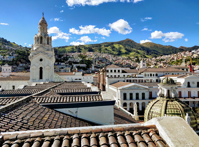 Quito: Colonial rooftops and a white church tower in Quito’s old town, green Andean hills rising behind