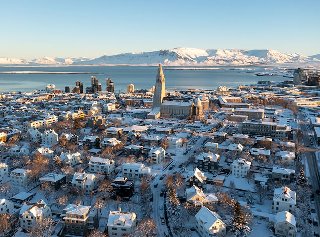 Reykjavík: Snow-covered Reykjavík from above, Hallgrímskirkja’s spire among pale rooftops, a white mountain across the bay