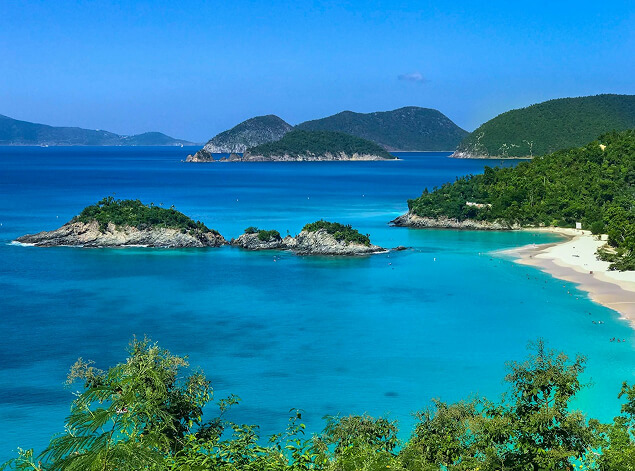 St. Kitts: A turquoise bay enclosed by green headlands, small wooded islets offshore and a pale beach at right