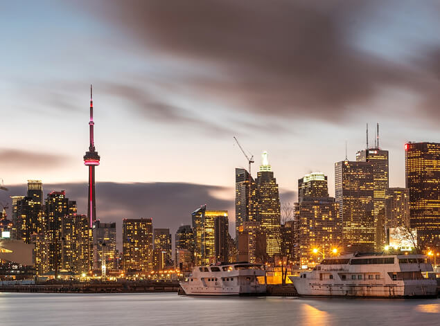 Toronto: The Toronto skyline at dusk from the harbour, the CN Tower lit among office towers under a long grey sky