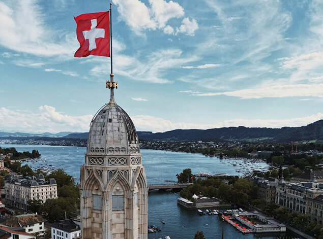 Zurich: A Gothic church spire flying the Swiss flag above the lake, wooded hills along the far shore