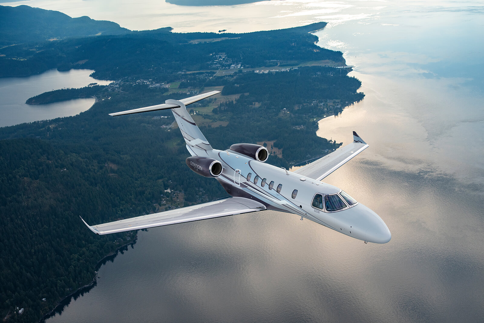 Cessna Citation CJ3 in flight along a forested coastline