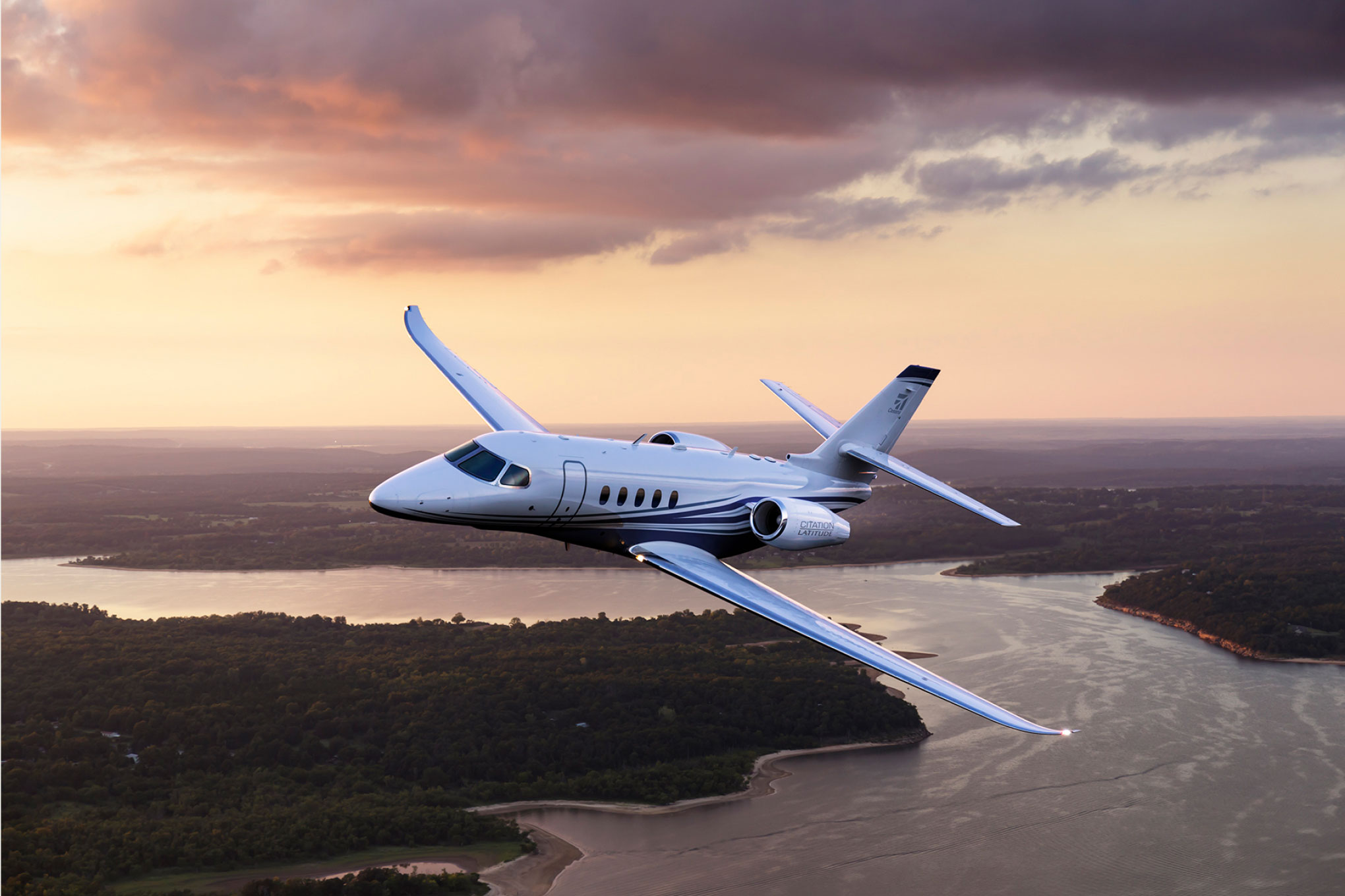 Cessna Citation Latitude in flight over a river at sunset