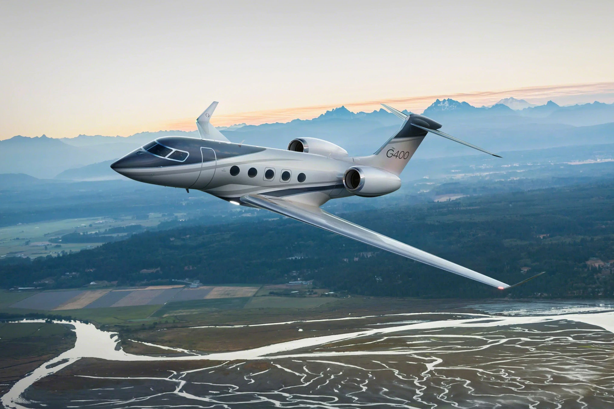 Gulfstream G400 in flight over a river delta below snow-capped mountains