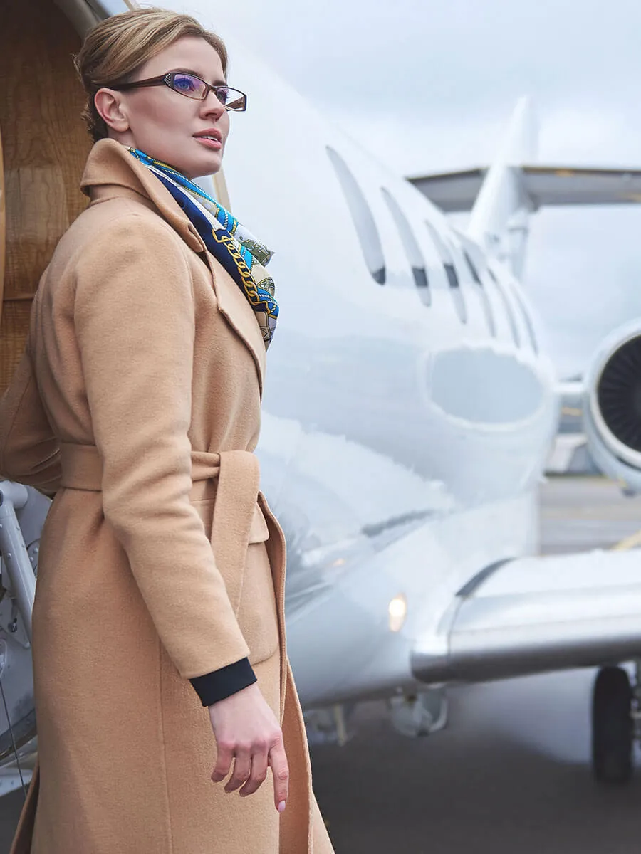 Traveler in a camel coat on the ramp beside a private jet