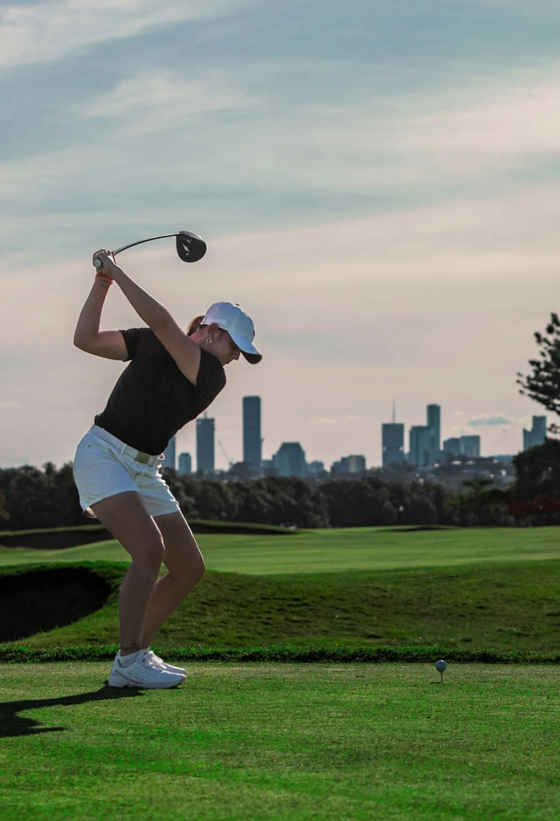 Golfer mid-swing on a fairway with a city skyline behind